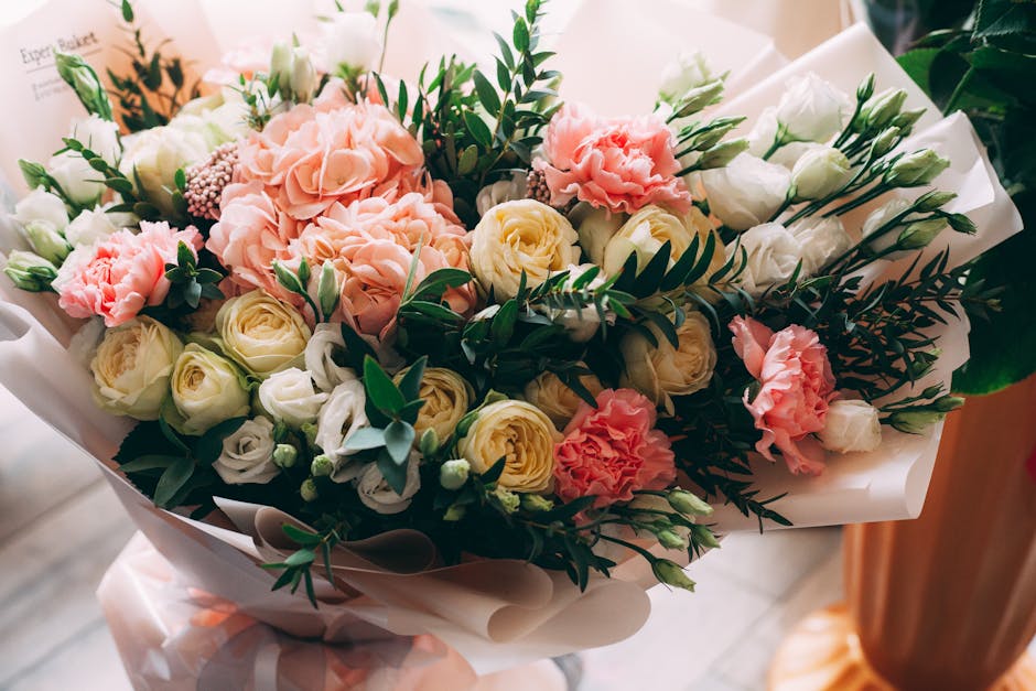 A floral arrangement featuring a variety of fresh flowers, including soft pink hydrangeas, creamy white roses, and delicate white lisianthus, complemented by dark green foliage with elongated leaves a