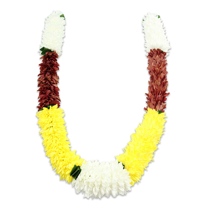 This U-shaped traditional floral garland is shown on a pure white background, its faint cast shadow emphasizing the careful curvature and dimensionality of the piece. At the top of each arm sits a dense, cylindrical block of creamy white, small tightly packed fabric petals that mimic the weightless fluff of miniature chrysanthemums or jasmine clusters; these sections provide a serene and auspicious opening. Directly below, each white block gives way to a concentrated band of maroon or dark reddish-brown, where similarly textured synthetic petals form a rich, grounding midsection. The longest, most prominent portion of the garland is a vibrant yellow sweep - many layered fabric blooms crafted to read like marigolds - which creates the pronounced lower curve of the U and lends the composition a cheerful warmth. Where the two yellow sections converge at the base, a broad central cluster of pure white chrysanthemum-style blooms forms a natural focal point, while small dark green leaf-like accents are interspersed at key transitions to accentuate colour changes and suggest foliage. The workmanship is clearly artificial in material: thousands of fabric petals and stitches hold the shape for longevity, suitable for repeated use in religious rituals, wedding ceremonies, temple offerings, or festival décor. As a mala, the colour choices are meaningful - white for purity, yellow for prosperity and morning blessings, maroon for devotion - and the garland would sit respectfully on an altar or be worn in procession during Diwali, Holi or traditional Hindu pooja events. Locally, this style is often requested by families across Deptford and neighbouring Lewisham, appearing at community gatherings and cultural events near Deptford Creek and the market area, where durability and ceremonial beauty are equally valued.