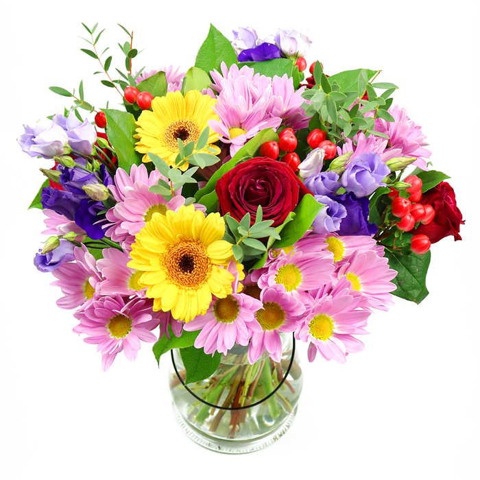 An abundant, hand-crafted bouquet rises from a clear glass vase, its colours vivid against a spotless white background, much like a bright splash of colour in a Deptford loft. At the centre of the arrangement, deep red roses open in lush spirals, their velvety petals layered tightly to create a sense of romance and depth. Sharing this focal point are two sunny yellow gerbera daisies with dark brown-orange centres, their wide, flat petals arranged like rays, giving the bouquet an instant feeling of joy. Around these primary blooms, generous sprays of soft pink daisies or chrysanthemums fan out, each flower characterised by numerous slender petals framing a small yellow core, building a halo of gentle, comforting colour. Interwoven among them are graceful purple and lavender lisianthus, their softly fluted, bell-shaped flowers lending sophistication and a cool-toned counterpoint to the warm reds and yellows. Dotting the arrangement, clusters of bright red hypericum berries appear like tiny polished marbles, offering a tactile contrast to the velvety and feathery petals. The whole bouquet is cradled in a variety of green foliage, from broad, darker leaves that ground the design to lighter, slender sprigs that lend lightness and movement, suggesting a freshly gathered garden feel. Through the transparent glass vase, carefully trimmed stems stand in clear, clean water, reflecting professional floristry skills and attention to detail. The bouquet feels celebratory yet welcoming, as though prepared for delivery across Deptford-perhaps to a gathering near the riverside or a cosy café off Deptford Broadway. Ideal for birthdays, thank-yous, or simply brightening a grey day, it radiates freshness, warmth, and the simple pleasure of beautifully arranged flowers.