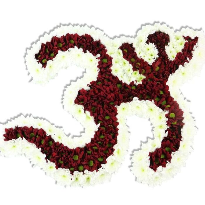 Set against a clean white background, this meticulously crafted floral Om (Aum) captures both devotion and design. The emblem's interior is composed of dense clusters of deep maroon to burgundy chrysanthemum-style blooms; the small-headed flowers are so tightly arranged they create a lush, velvety plane, and the unexpected lime-green eyes at many centres animate the dark field like tiny embers. Surrounding and defining the symbol is a generous outline of pristine white spray chrysanthemums, their compact blooms forming a ribbon of light that makes every loop and downward stroke unmistakable. A faint, natural drop shadow beneath the composition gives the whole piece a three-dimensional presence, as if the emblem gently lifts from its white stage. The visual texture is tactile - you can almost sense the cool, satiny petals and the faint, grounding fragrance that rises from the red cores, a scent suited to quiet reflection. This arrangement reads as a respectful tribute for religious observance, temple offerings, meditation events or memorial services; its balance of colour and form conveys peace and concentrated care. As a Deptford florist who knows the neighbourhood around Deptford Church Street and New Cross Gate, I imagine delivering a piece like this to a community gathering or placing it for an intimate ceremony near Deptford Market Yard, where local families recognise careful, handcrafted floral work. The craftsmanship is both artistic and ceremonial, a floral prayer shaped for moments of inward attention.